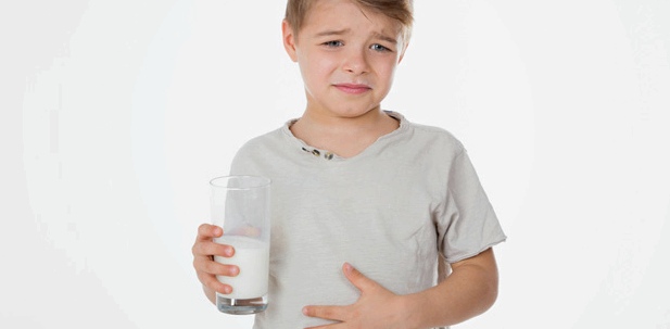 Ein Junge hat ein Glas Milch in der Hand und hält sich den Bauch