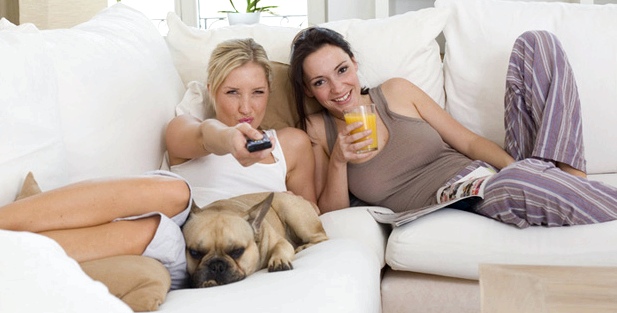 Zwei Freundinnen sitzen auf einer Couch und sehen fern