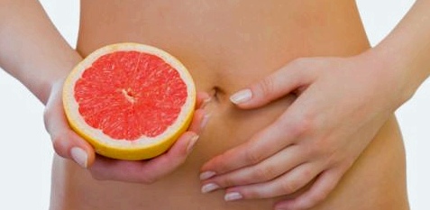 Eine Frau hält sich eine Grapefruit vor den Bauch