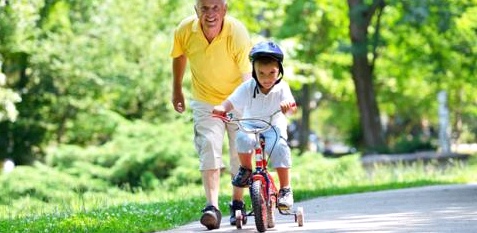 Ein kleiner Junge fährt Dreirad und sein Großvater läuft hinter ihm her
