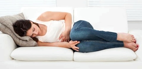 Frau liegt mit Bauchschmerzen auf dem Sofa